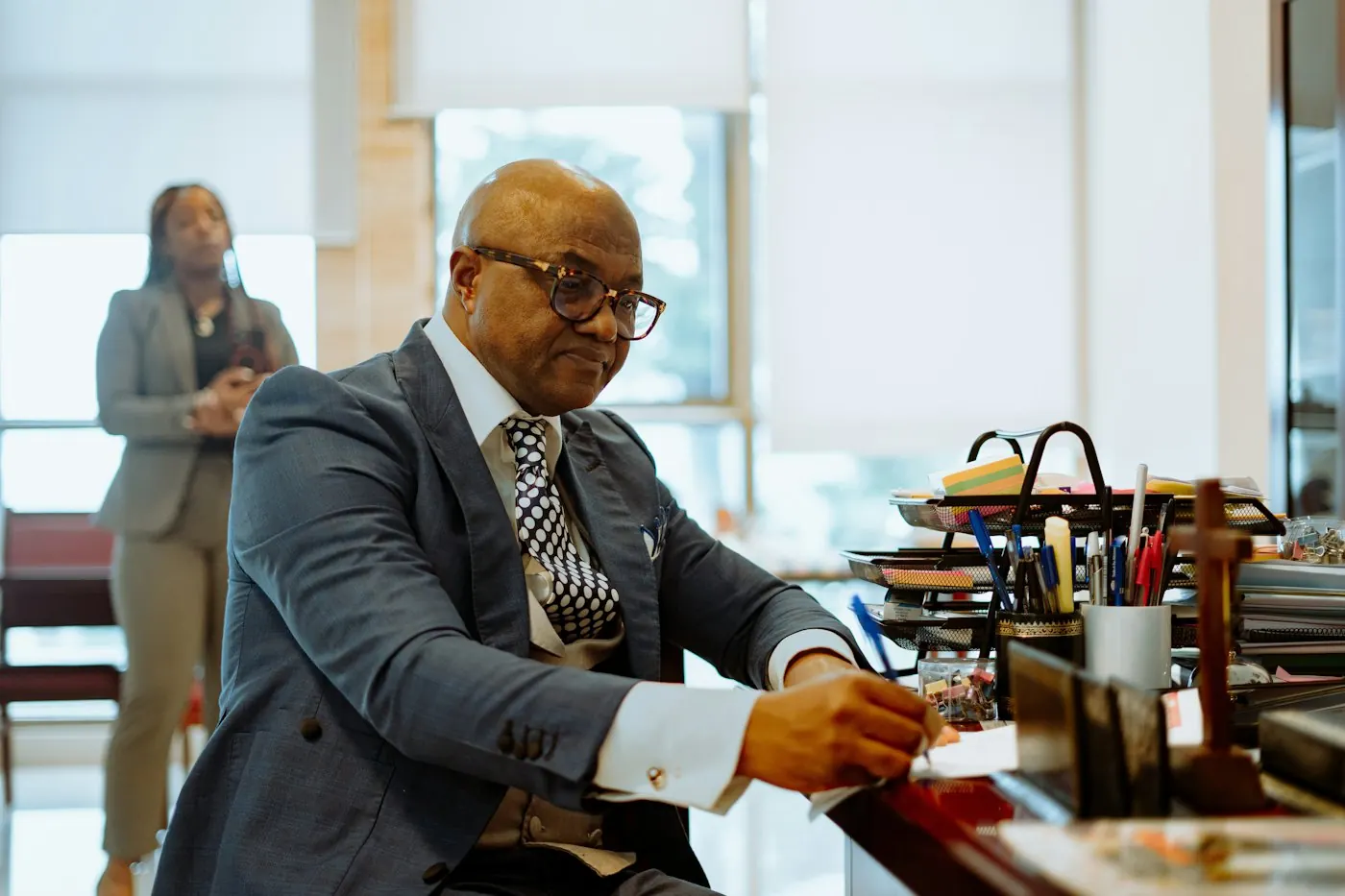 An attorney working at his desk while a colleague reviews a file behind him
