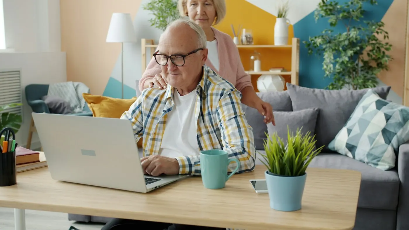 An older couple signing documents together on a laptop at home